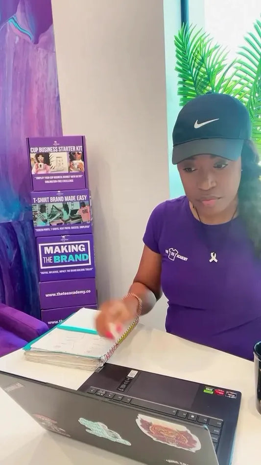Coach Tee at her laptop with The Tee Academy t-shirt starter boxes behind her